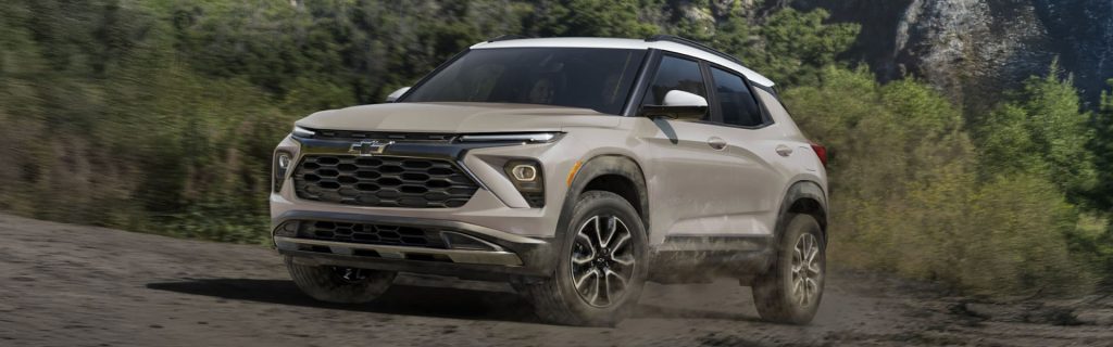 White Chevrolet SUV driving on a dirt road surrounded by greenery.